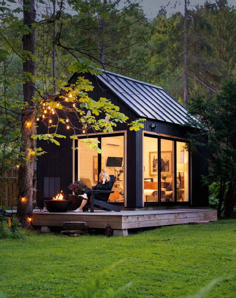 Modern black cabin with fire pit and string lights in the forest
